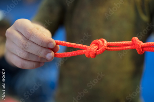 bright orange climbing rope with knots in the hands of a child in green t shirt