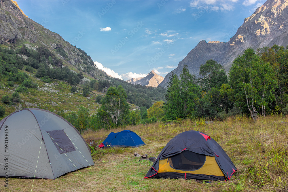 tourist tents are in the meadow in the morning on green grass surrounded by the mountain peaks in summer
