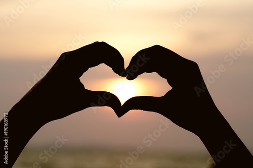 Silhouette hand in heart shape with sunrise in the middle and beach .as background Valentine concept with copy spaces for your text or design.