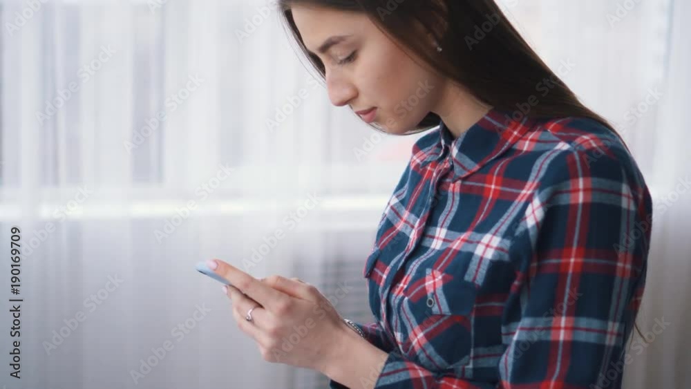 Sociable young girl texting on smartphone in living room Sociable young girl texting on smartphone in living room