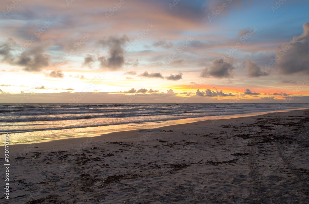 view of blue sky and full of morning clouds on a beach with orange sun colors.