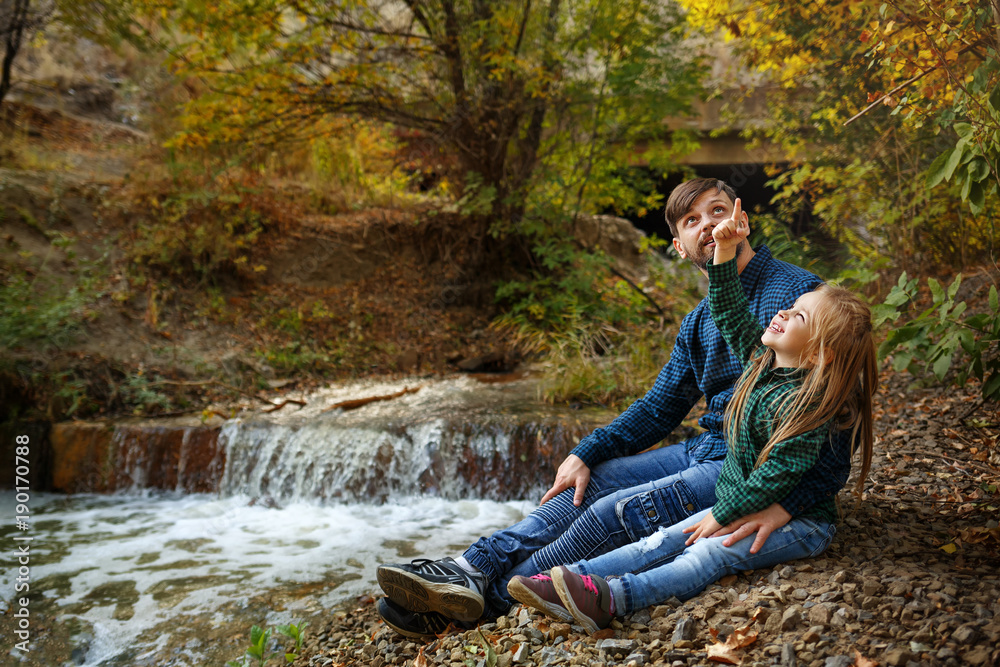 Father and daughter are sitting by the waterfall