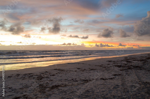 view of blue sky and full of morning clouds on a beach with orange sun colors.