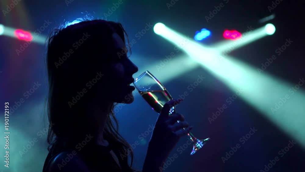 Silhouette of a young girl who drinks champagne at the party in the dark on the background of flashing lights, slow motion. Silhouette of a young girl who drinks champagne at the party in the dark on the background of flashing lights, slow motion.