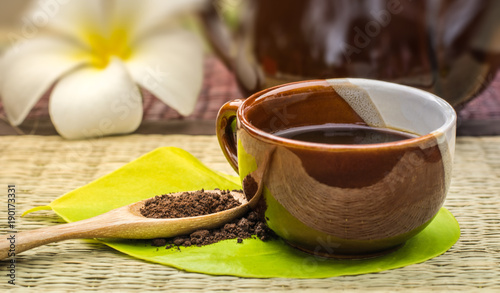 Coffee lover.Coffee cup on green leaf with roasted coffee on wooden spoon.Background is a white plumeria and coffee pot.