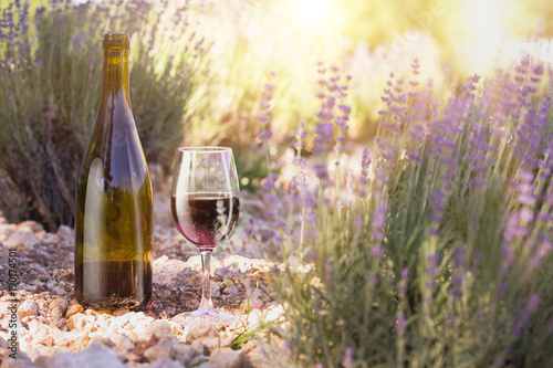 Red wine bottle and wine glass on the ground. Bottle of wine against lavender landscape. Sunset over a summer lavender field in Provence, France.
