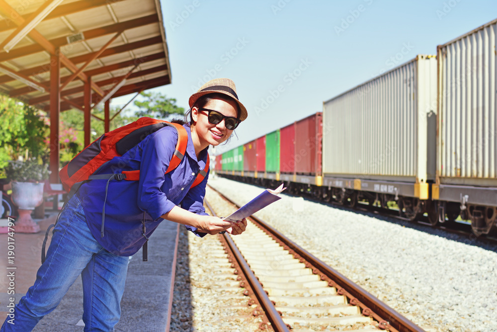 Young woman traveler with backpack and hat holding map with train background