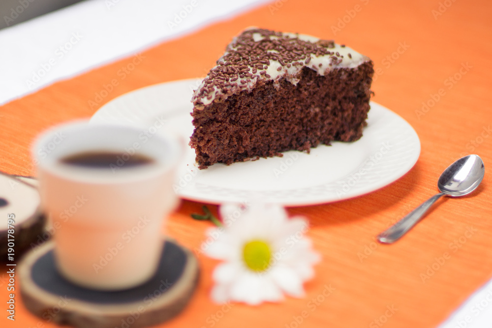 Chocolate cake slice with white chocoalte cream in plate with cup of coffee