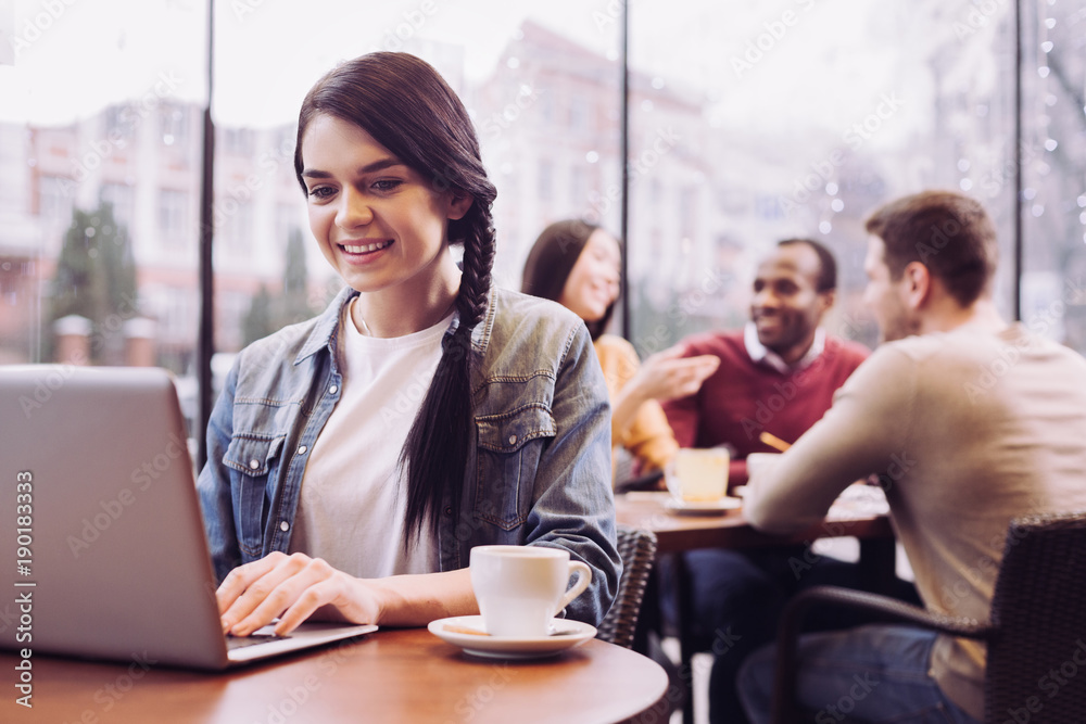 Digital communication. Jolly enthusiastic happy woman staring at the screen while looking down and posing at cafe Digital communication. Jolly enthusiastic happy woman staring at the screen while looking down and posing at cafe