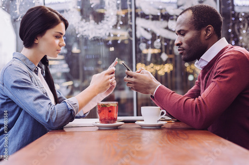 Negative effect. Smart pleasant modern couple drinking beverages while sitting and looking at the phones