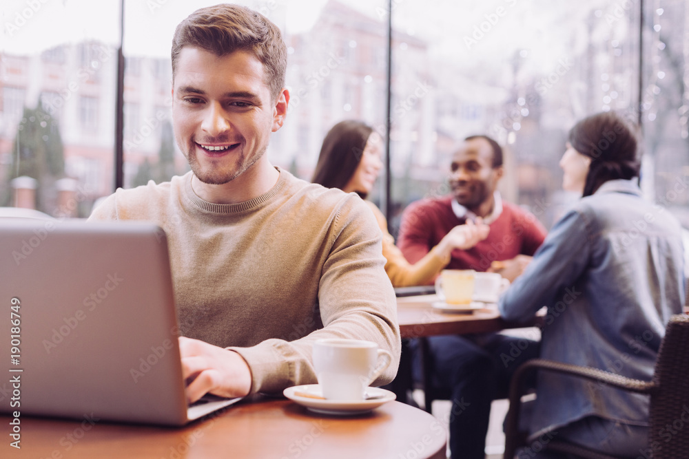 Online game. Appealing cute nice man typing on laptop while enjoying coffee and emerging in virtual world Online game. Appealing cute nice man typing on laptop while enjoying coffee and emerging in virtual world