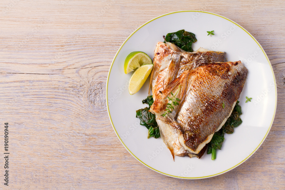 Roasted sea bream with spinach. Dorado or dorada fish fillet on white plate Roasted sea bream with spinach. Dorado or dorada fish fillet on white plate