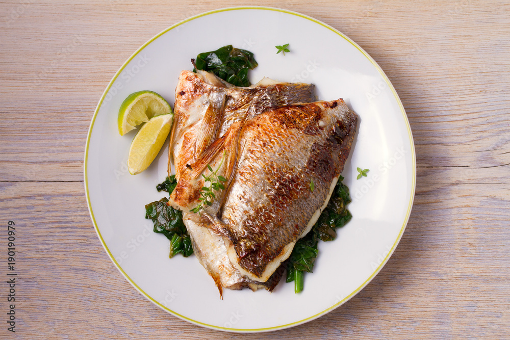 Roasted sea bream with spinach. Dorado or dorada fish fillet on white plate Roasted sea bream with spinach. Dorado or dorada fish fillet on white plate