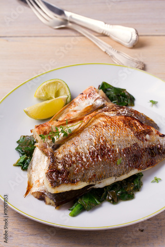 Roasted sea bream with spinach. Dorado or dorada fish fillet on white plate