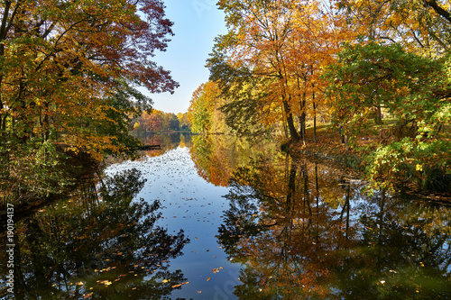 Słoneczny jesienny krajobraz - park w złotych kolorach, wodny trakt z malowniczymi wysepkami wokół, pożółkłe liście dominują w obrazie