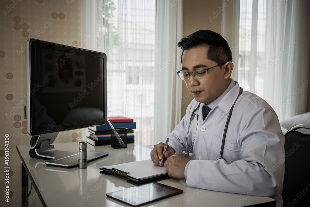 Doctor is working with documents in front of his computer in his workplace.