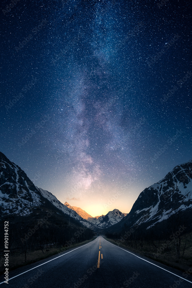 Fototapeta Milky way glowing above a road leading to distance in a mountain valley.