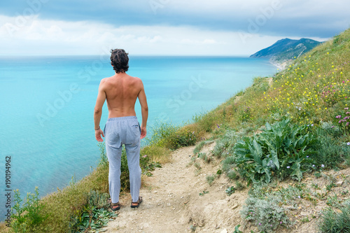 Handsome man standing on hill and looking on sea. Side back.