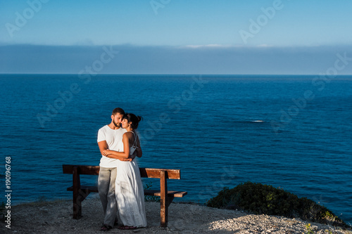 Couple in love at dawn by the sea. Honeymoon. Honeymoon trip. Boy and girl at the sea. Man and woman traveling. Couple hugs. Couple kissing. Newly married couple. Lovers. Holiday romance