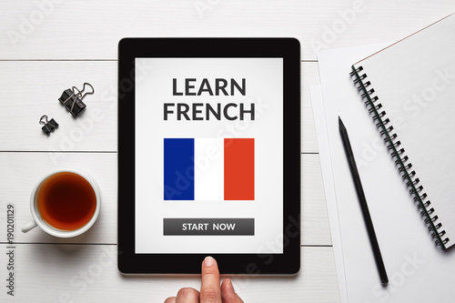 Learn French concept on tablet screen with office objects on white wooden table. All screen content is designed by me. Flat lay