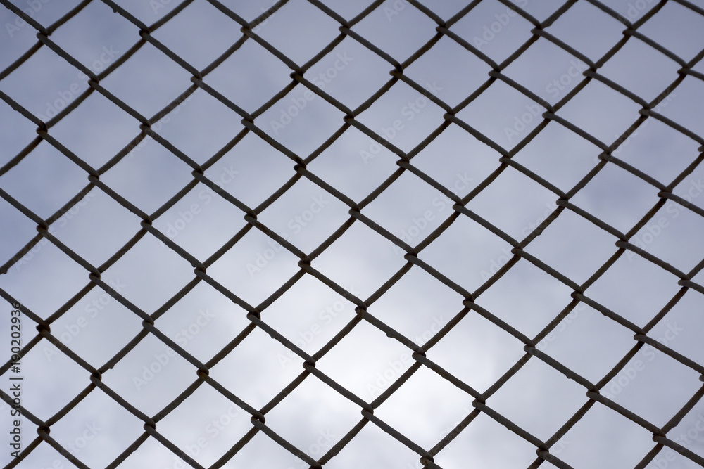 several rows of metal mesh with square cells used as a guard, in the background in the background of the sky the lines from another grid are out of focus several rows of metal mesh with square cells used as a guard, in the background in the background of the sky the lines from another grid are out of focus