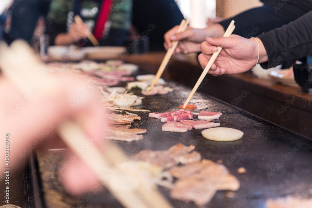 Fototapeta premium hand holding chopstick grilled meat on hot pan
