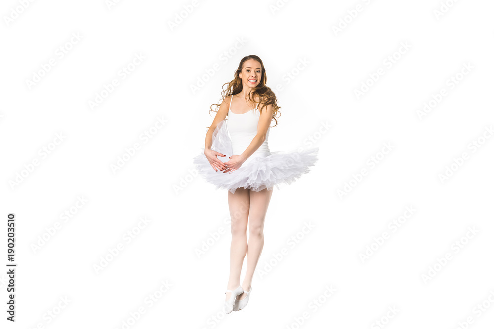 Naklejka premium happy young ballerina dancing and smiling at camera isolated on white