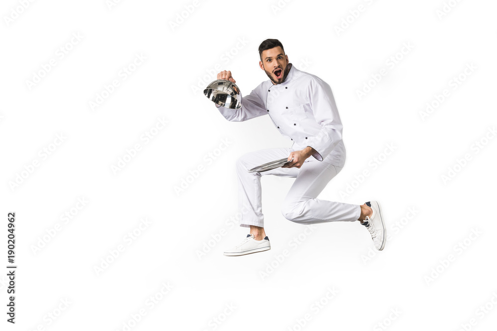 surprised young chef opening dish and looking at camera isolated on white surprised young chef opening dish and looking at camera isolated on white