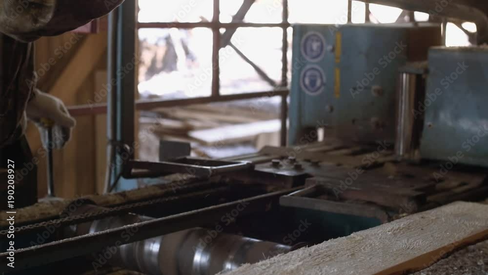 Unrecognisable woodworker manages industrial saw machine with timber log at sawmill factory, sunny day outside Unrecognisable woodworker manages industrial saw machine with timber log at sawmill factory, sunny day outside