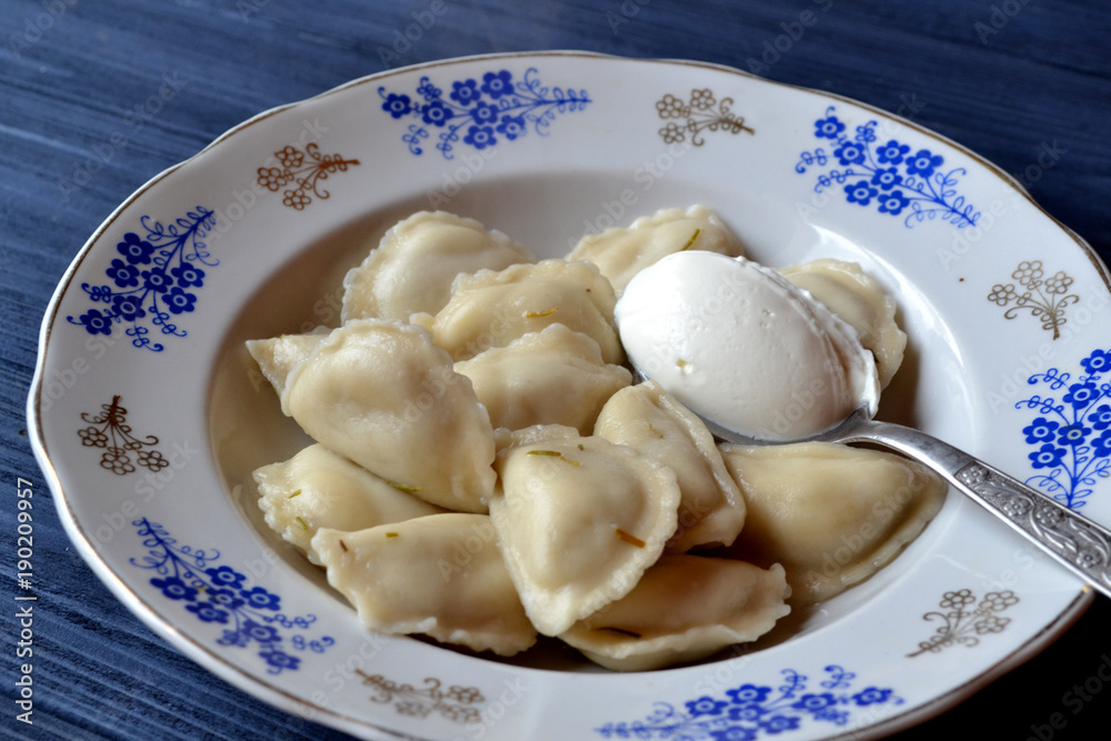 Dumplings with sour cream in the plate on the dark blue wooden table.