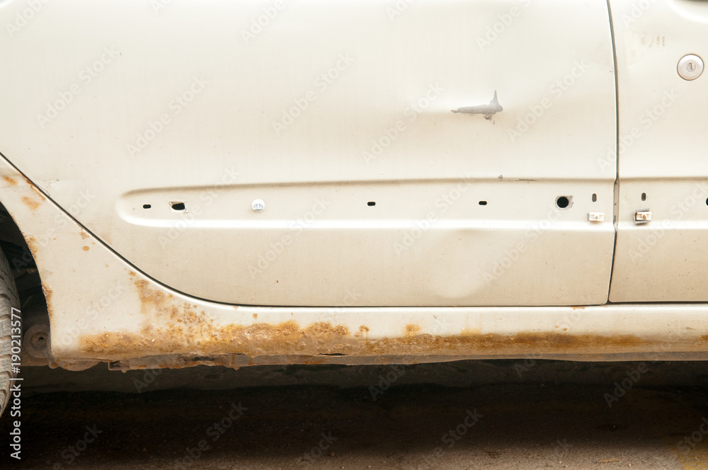 Damaged white car with scratched paint and rust with holes at the bottom of the floor