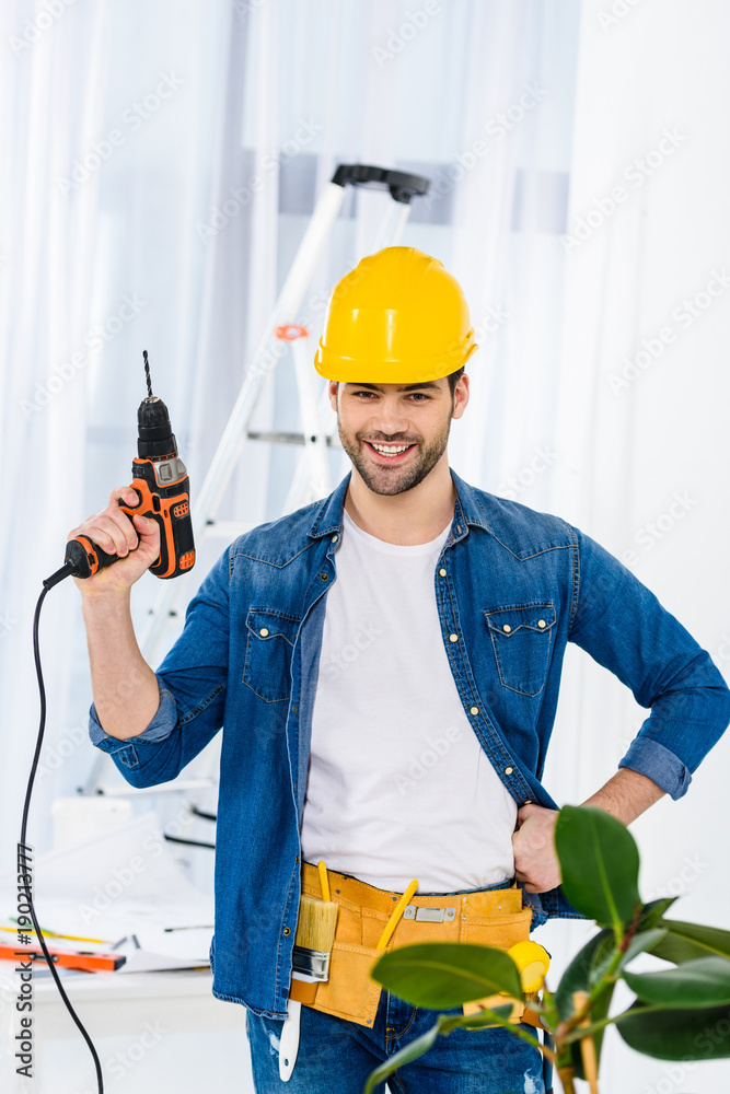 smiling handsome man standing with drill and looking at camera smiling handsome man standing with drill and looking at camera
