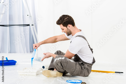 side view of handsome man pouring paint into tray