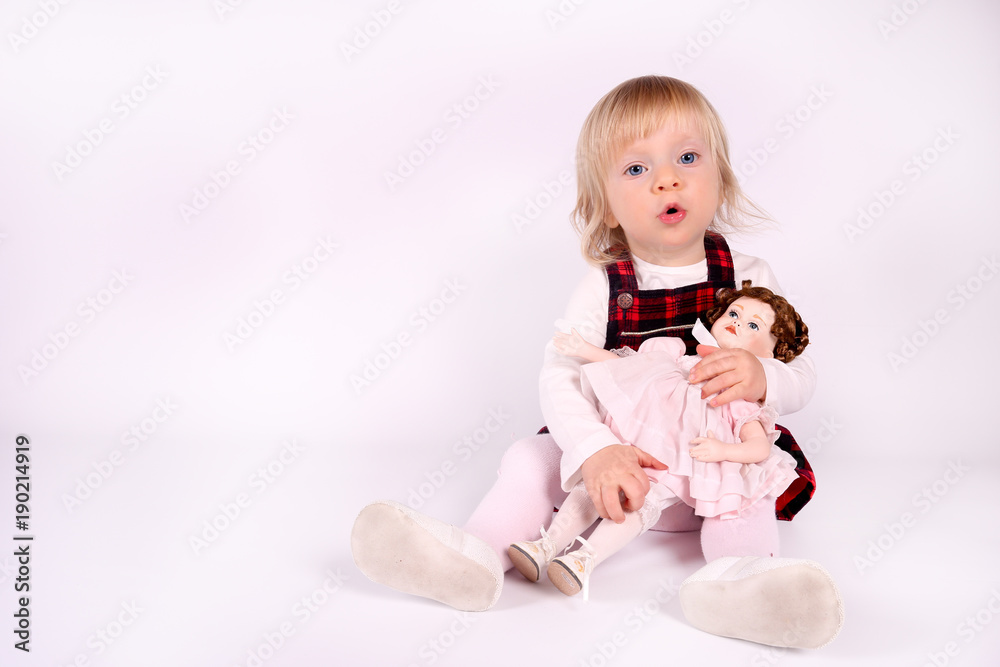 Little blonde toddler girl with big Blue Eyes in red dress play with old doll. Sitting on the floor, white background. Portrait, close-up isolated Little blonde toddler girl with big Blue Eyes in red dress play with old doll. Sitting on the floor, white background. Portrait, close-up isolated