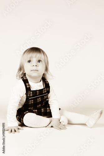 Little blonde toddler girl with big Blue Eyes in red dress looking up.Sitting on the floor, white background. Portrait, close-up isolated , Sepia Tone