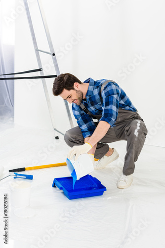 smiling man pouring paint from bucket into plastic paint tray