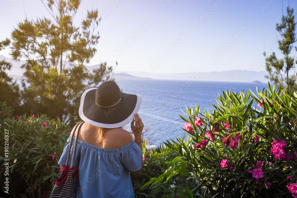 woman in dress holding a straw hat and looking to a blue sea