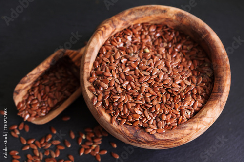 Organic flax seed in wooden bowl on black slate background copy space. Linum usitatissimum