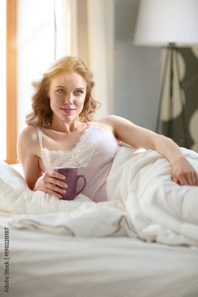 Young woman drinking cup of coffee or tea while lying in bed. Young woman drinking cup of coffee or tea while lying in bed.