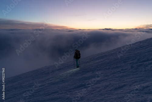 Hiking woman with headlamp on snow in Slovak mountains above clouds after sunset in winter