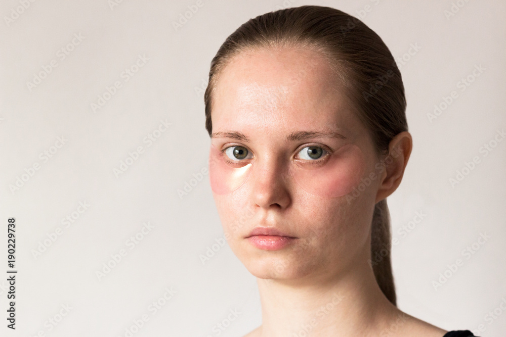 Fototapeta premium Girl uses pink hydrogel patches under her eyes. Cosmetology, self-care.
