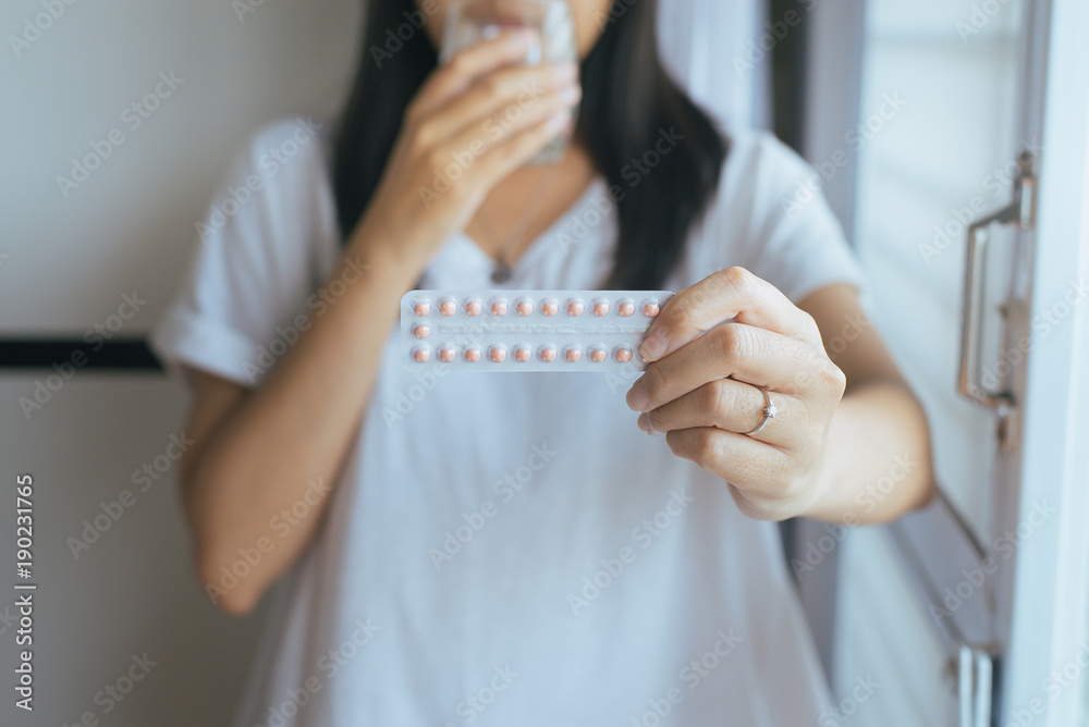Close up of hand female holding birth control pill and a glass of water,Concept for contraception