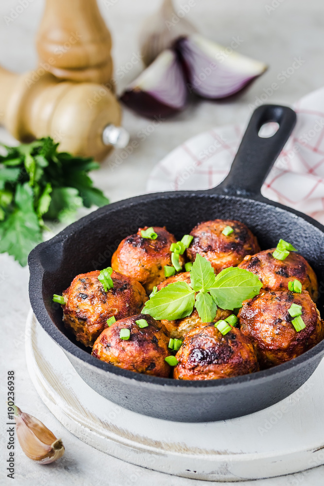 Baked Italian herb meatballs in cast iron skillet on white stone background. Selective focus, copy space.