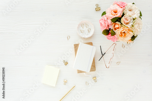 Women's workspace with pink and beige roses flowers bouquet, accessories, diary, glasses on white background. Flat lay, top view trendy fashion feminine background. Beauty blog concept.