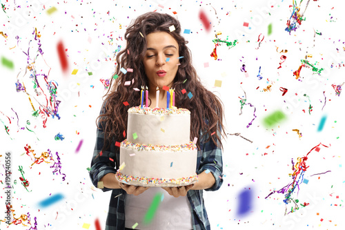 Teenage girl blowing candles on a birthday cake with confetti streamers flying around her