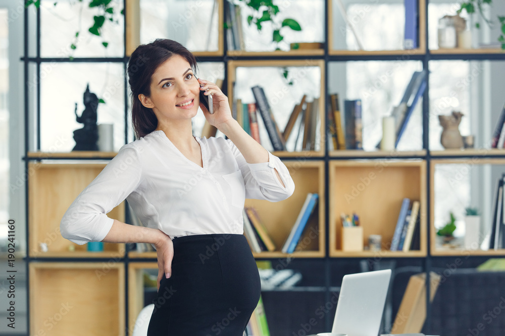 Pregnant business woman working at office motherhood standing answering phone call Pregnant business woman working at office motherhood standing answering phone call