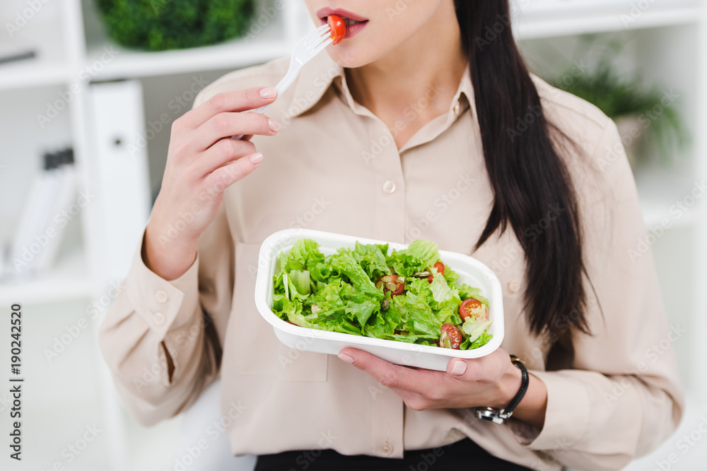 partial view of businesswoman eating take away salad for lunch in office
