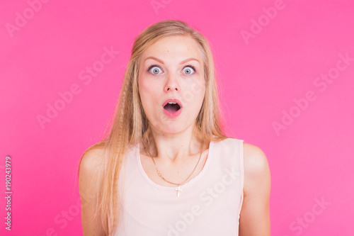 Surprised young woman over pink background. Looking at camera