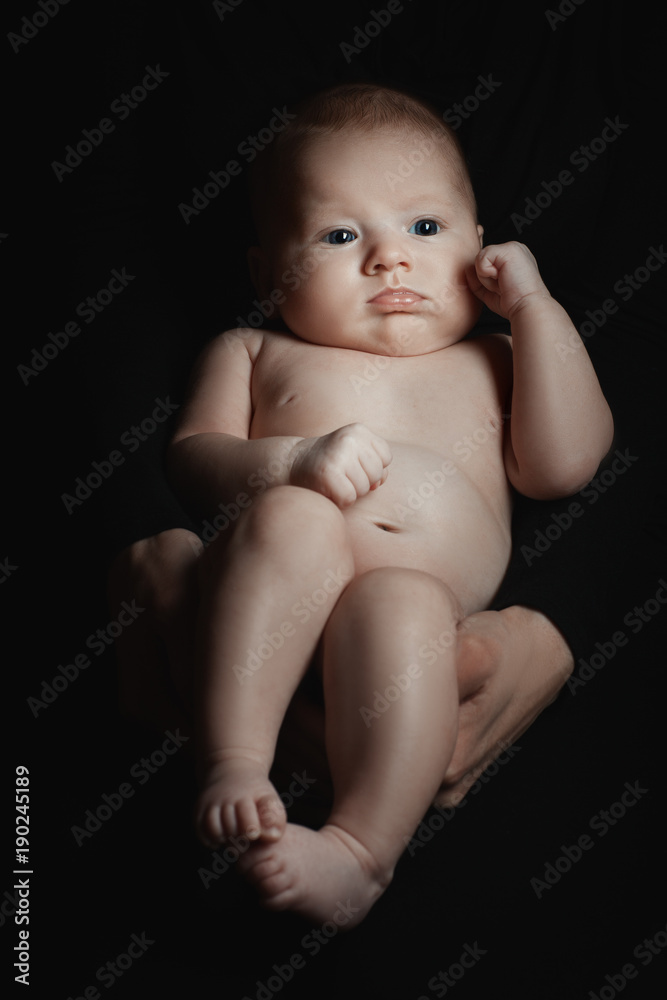 Portrait of a baby girl in the dark. Men's hands hold the child Portrait of a baby girl in the dark. Men's hands hold the child