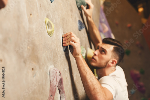 Young man climbing artificial rock wall at gym